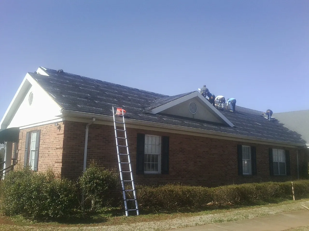 Crew tearing shingles off a brick ranch roof with a ladder set — Emergency Roof Repair work by our crew in Neotsu