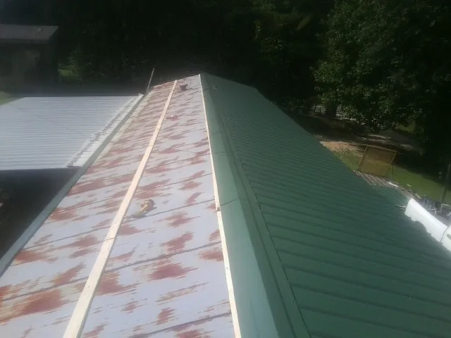 Old rusted panels beside newly installed green metal roofing — Wind Damage Roof Repair by Roofing Brothers in Neotsu