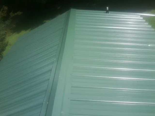 New green metal panels meeting at the ridge of a roof — Flat Roof Repair work by our crew in Neotsu