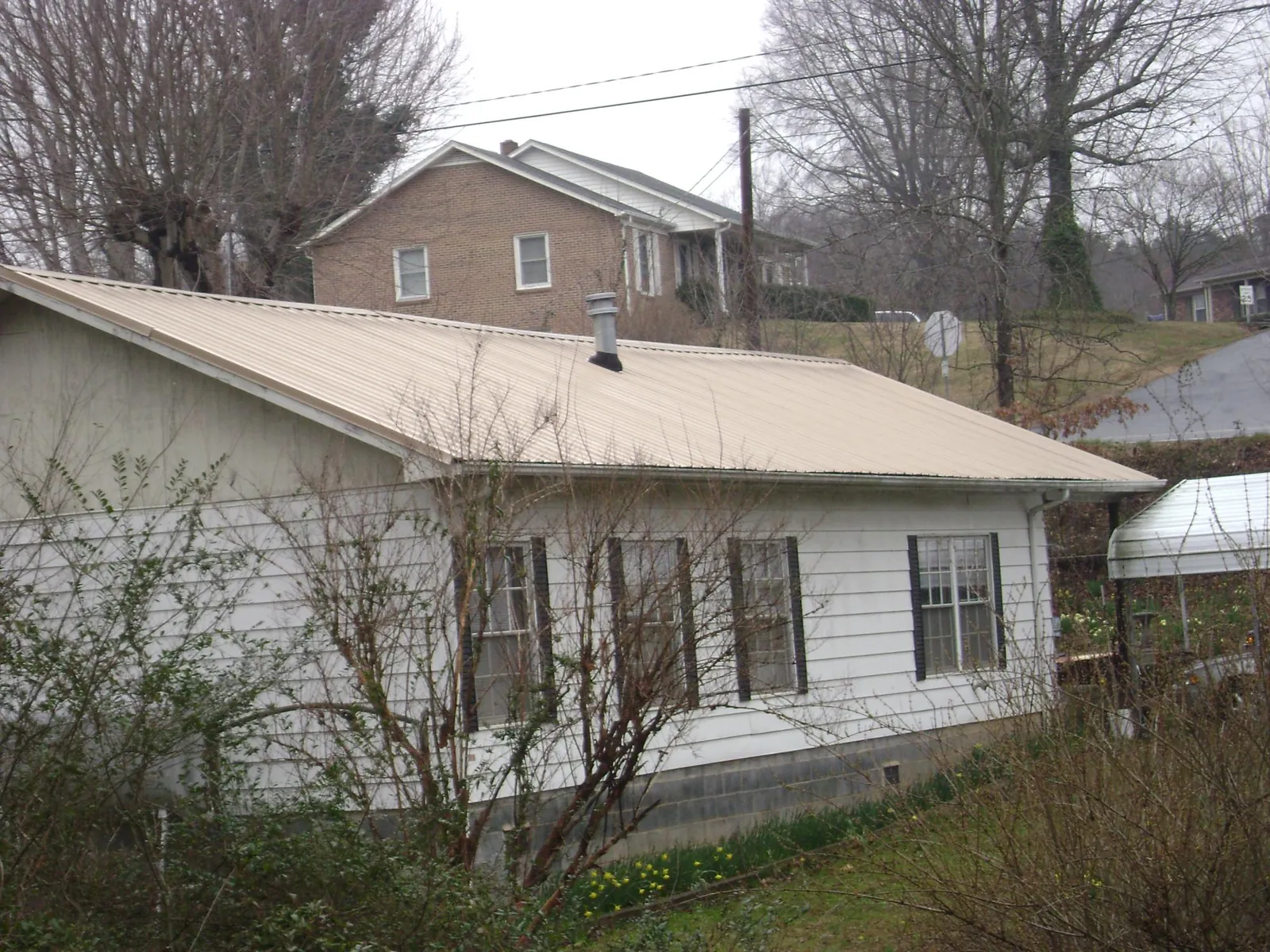 Tan metal roof on a white sided house set into a hillside — Commercial Roofing by Roofing Brothers in Neotsu